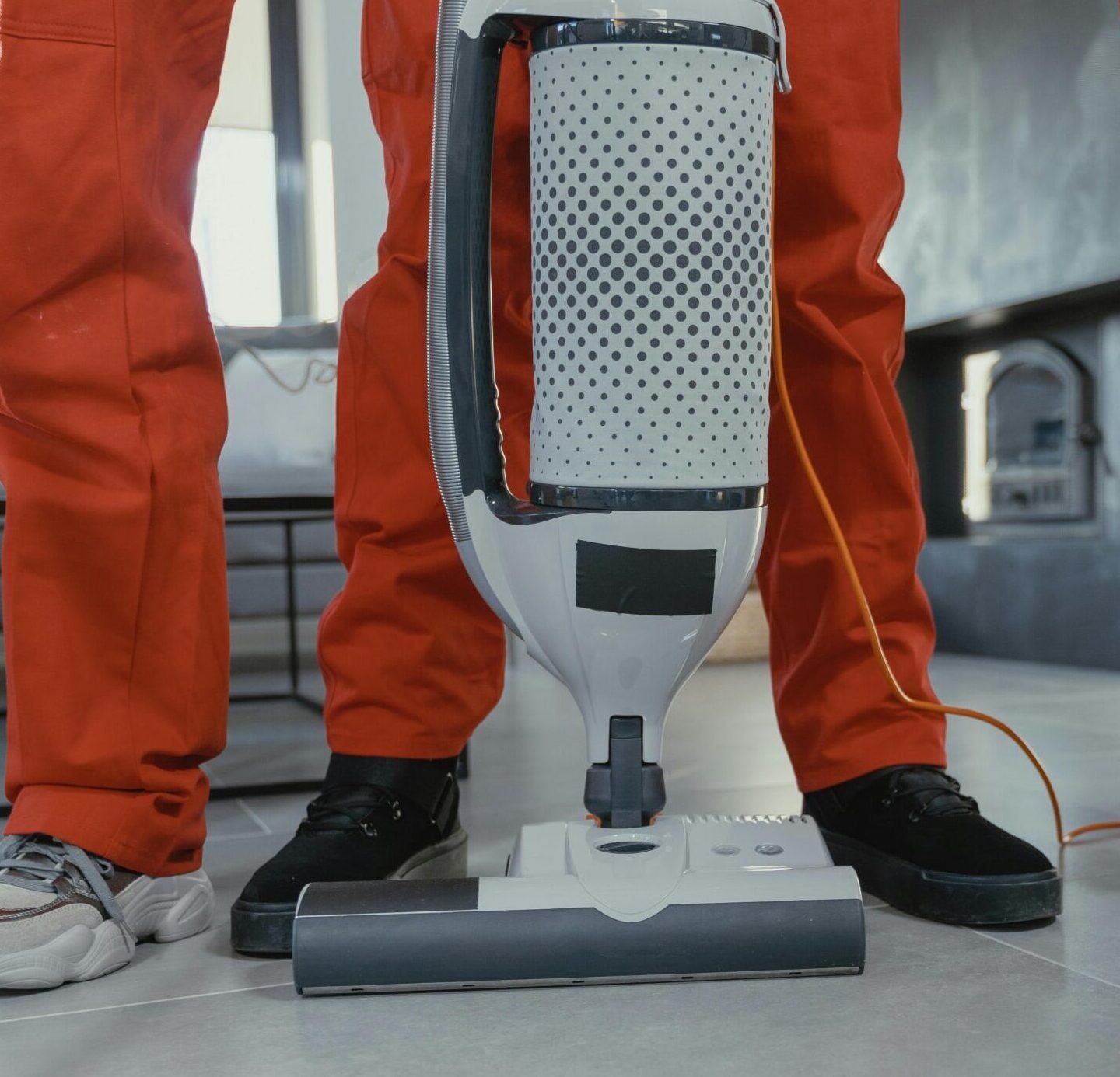Team of professional cleaners in red uniforms using a vacuum cleaner indoors.